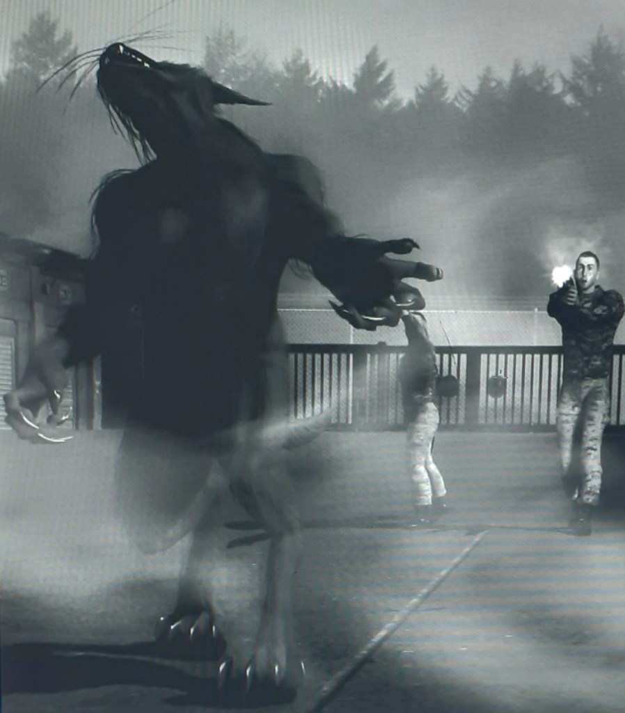 Recreation of bipedal werewolf being fired upon by two military staff at a gated checkpoint. The werewolf seems to be recoiling from gunshot.